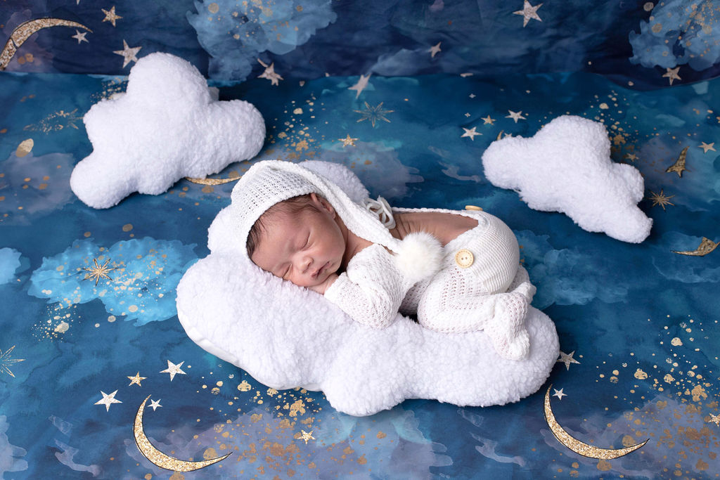 A newborn baby wrapped in cream knit, eyes closed, sleeping peacefully against a soft warm backdrop.